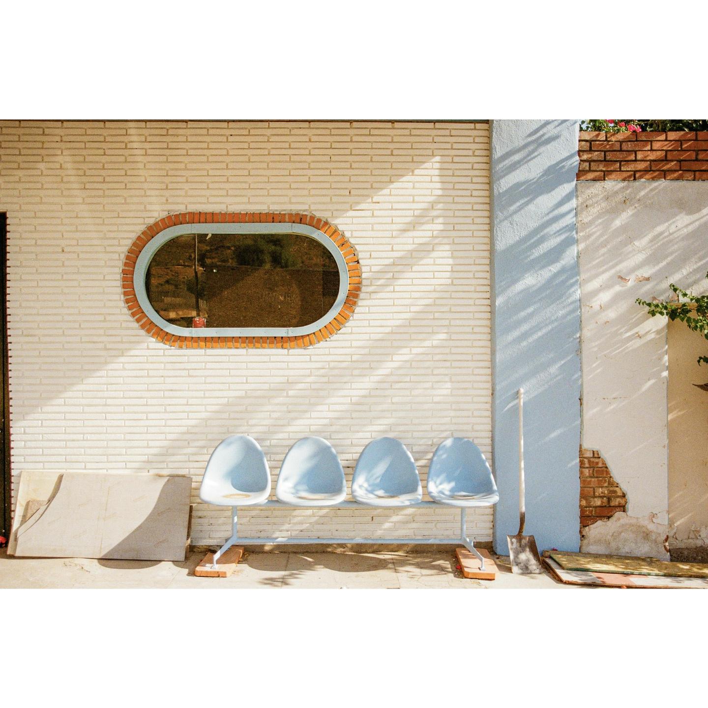 Four light blue chairs are lined up against a white brick wall with an oval window.