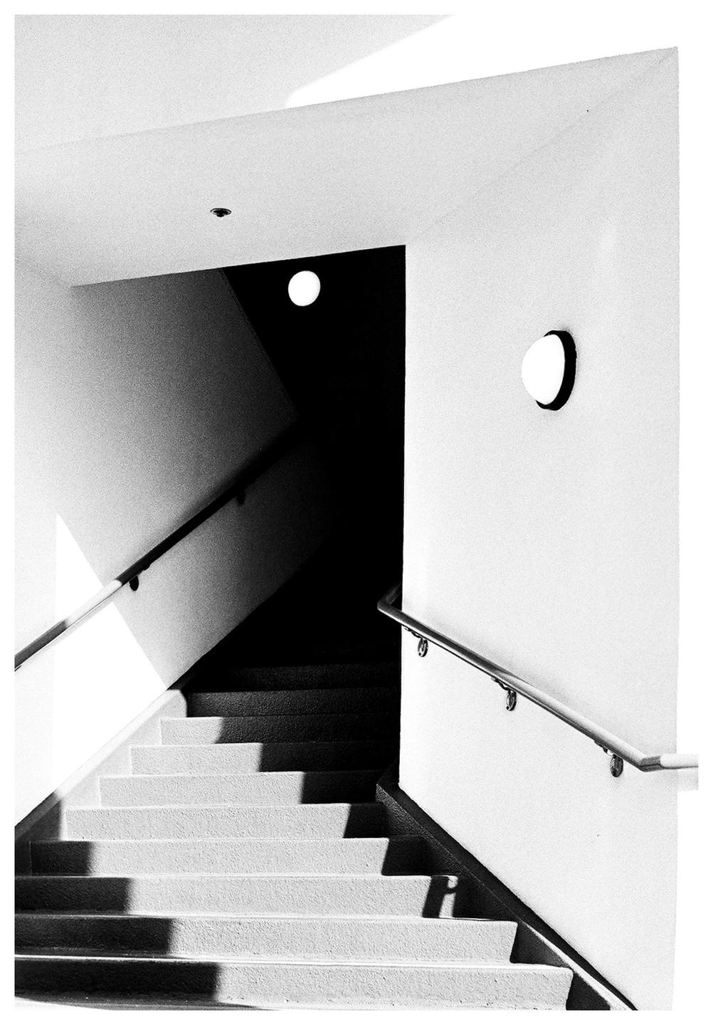 A black and white photograph shows a staircase with handrails and two circular lights on the walls.