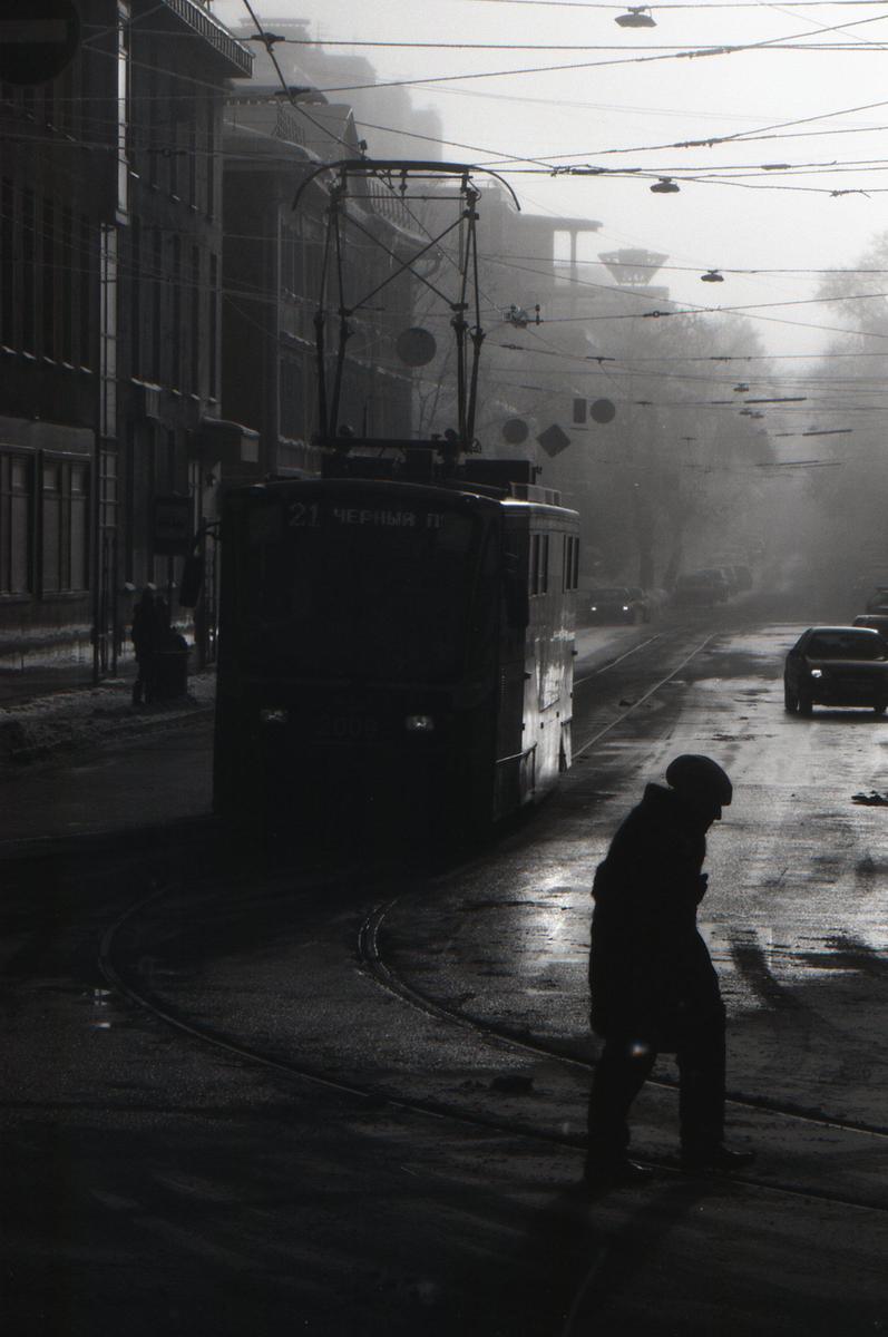 A person walks on a wet street next to a tram on a hazy day.