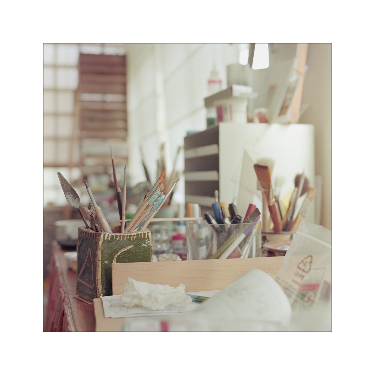 A collection of art supplies, including paintbrushes and palette knives, are arranged on a cluttered desk.