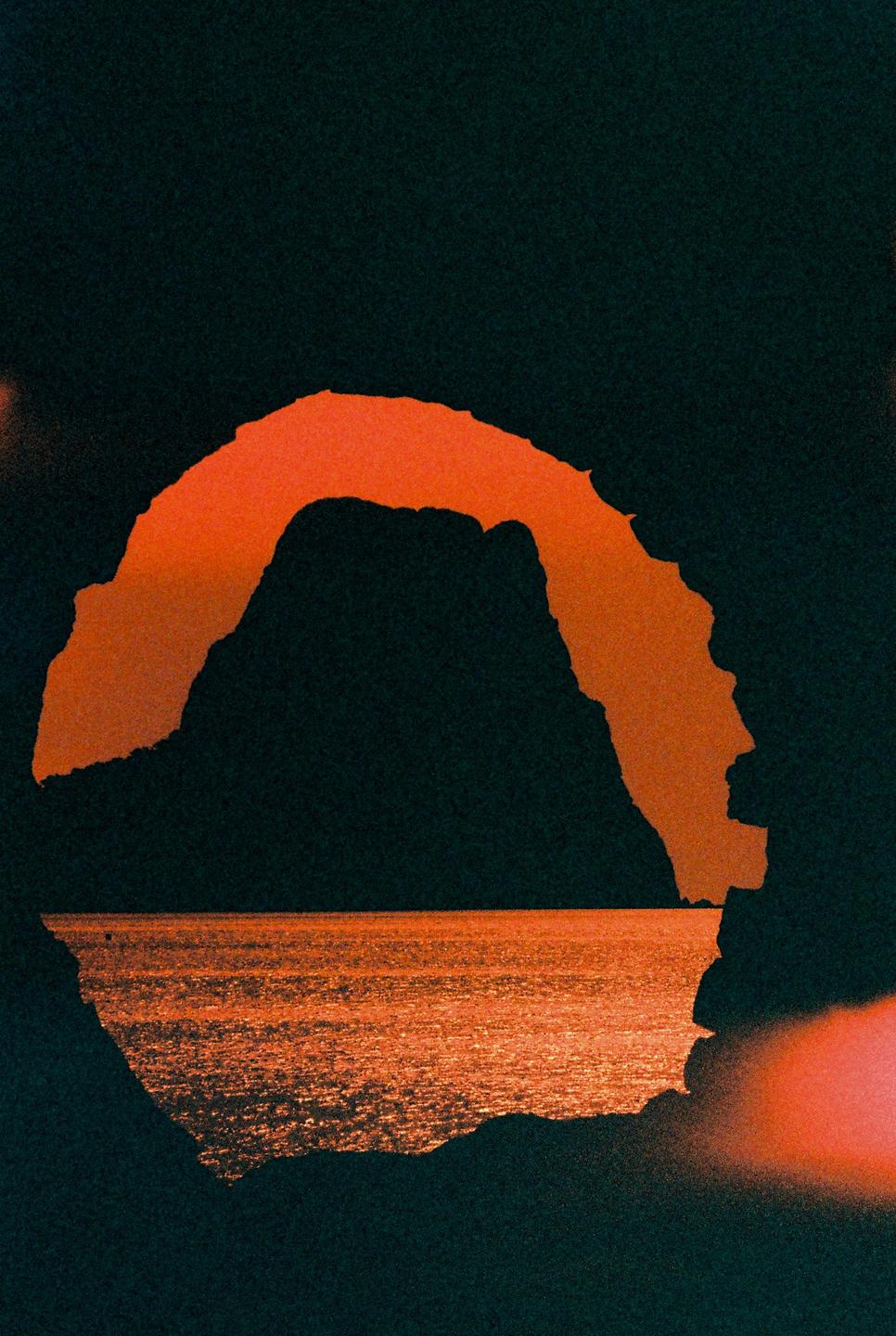 A dark silhouette of a mountain and sea is visible through a cave opening during sunset.