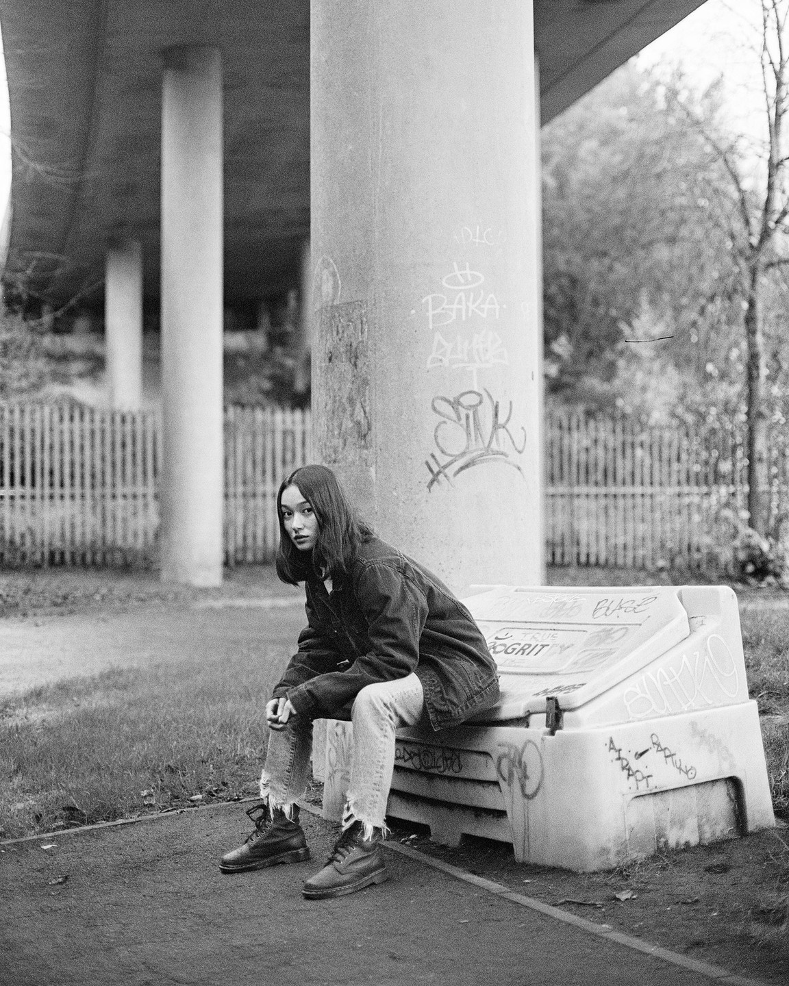 A woman sits on a concrete barrier under an overpass.