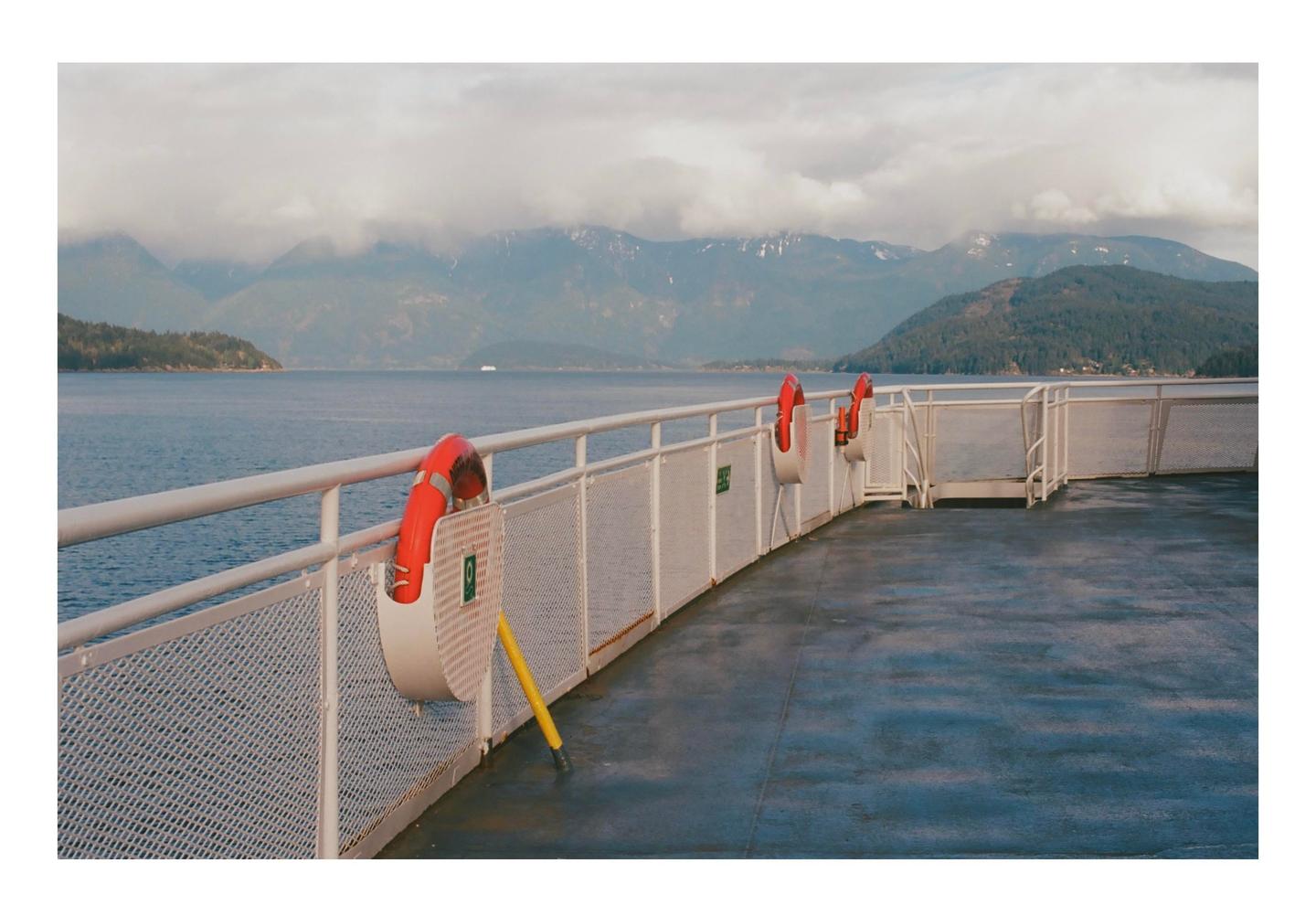 A ferry deck with life preservers is visible in the foreground, with mountains and water in the background.