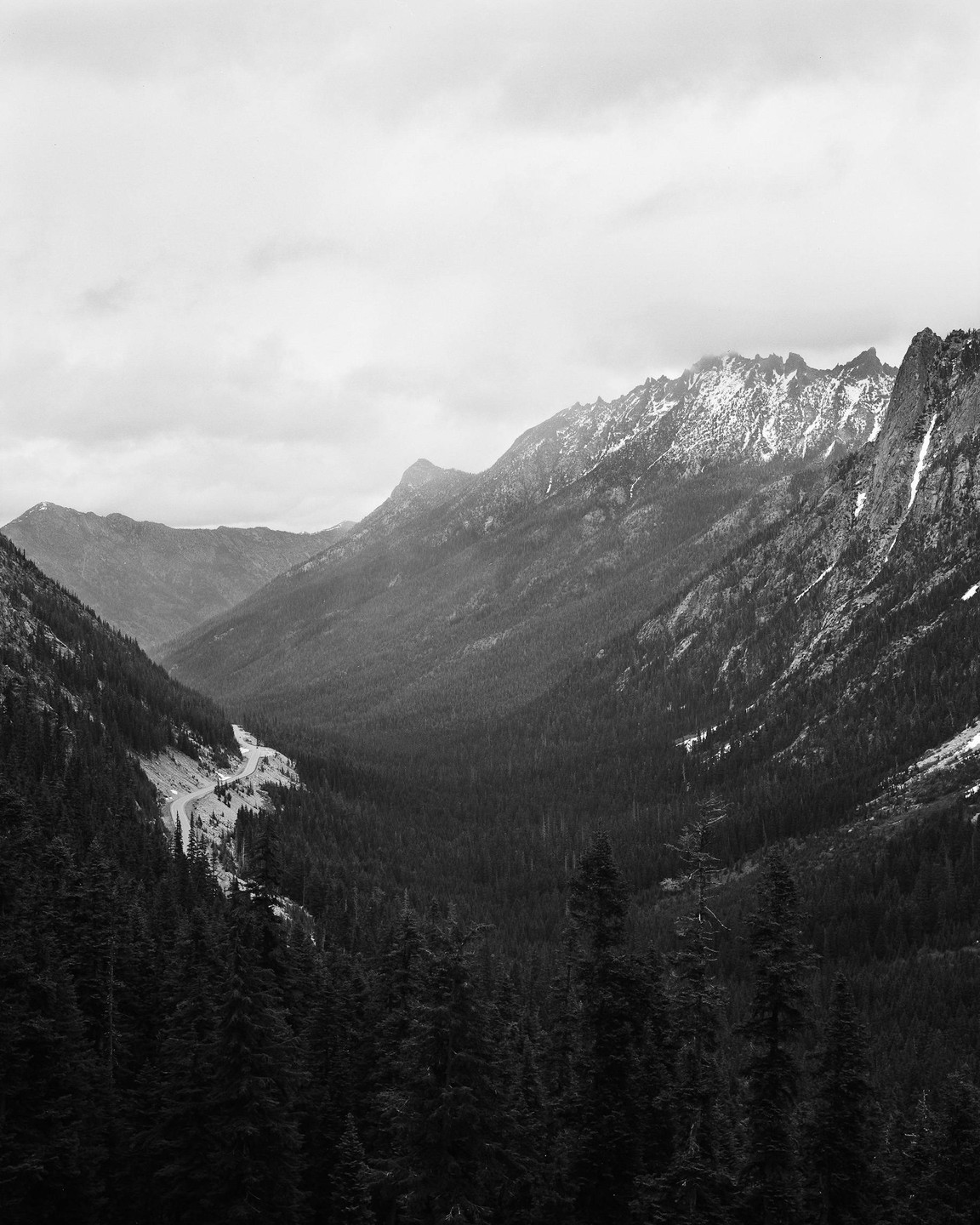 A winding road cuts through a valley surrounded by mountains and dense forest.