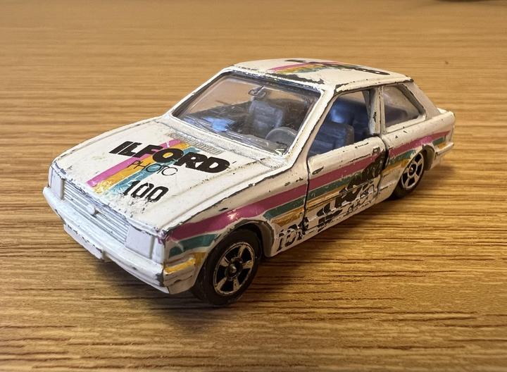 A white toy car with colorful stripes and text on its hood is sitting on a wooden surface.