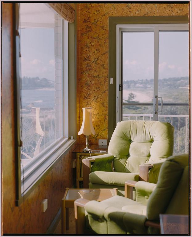 Sunlight streams into a room with two green armchairs and a view of the ocean.