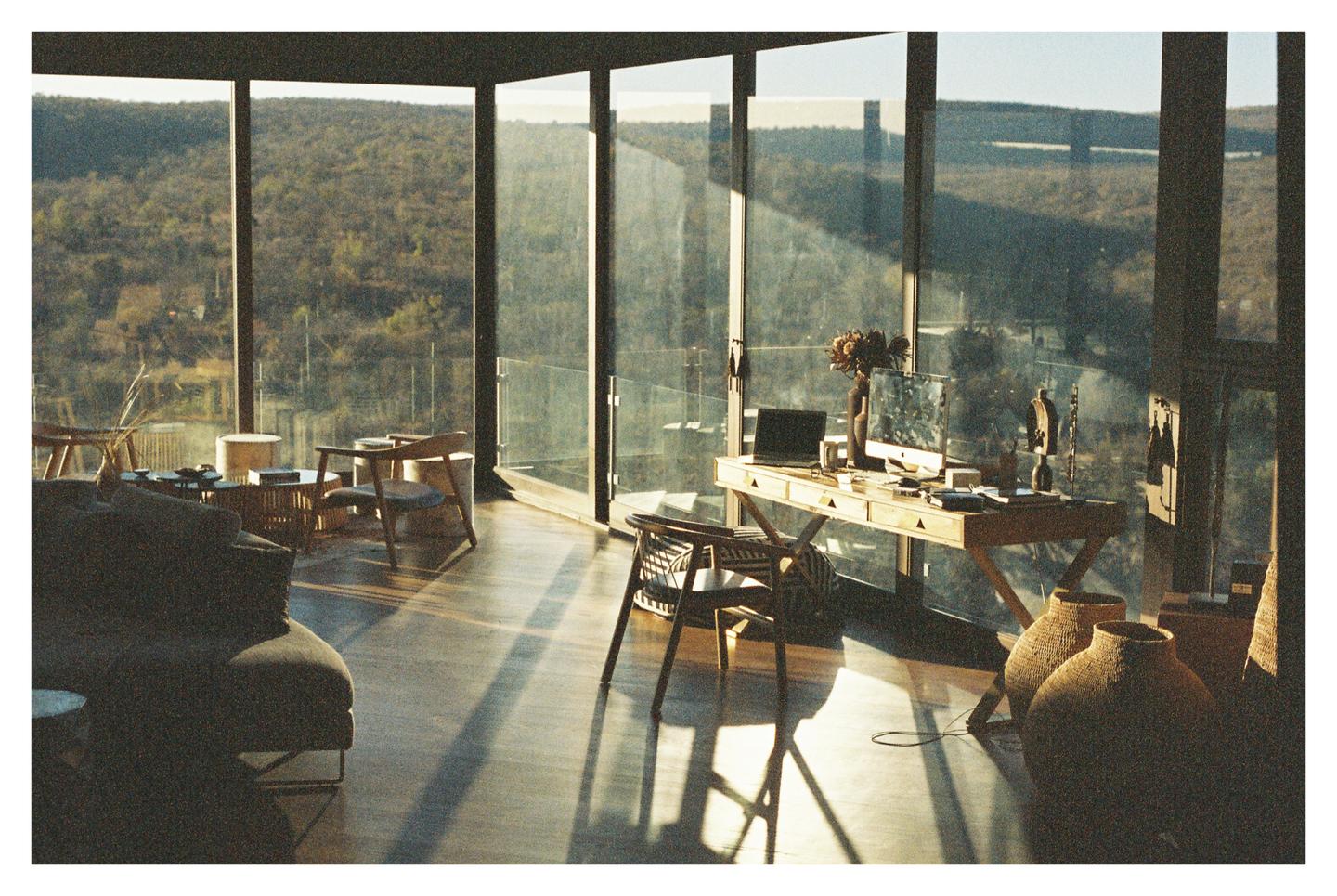 Sunlight streams into a modern room with large windows overlooking a wooded landscape.