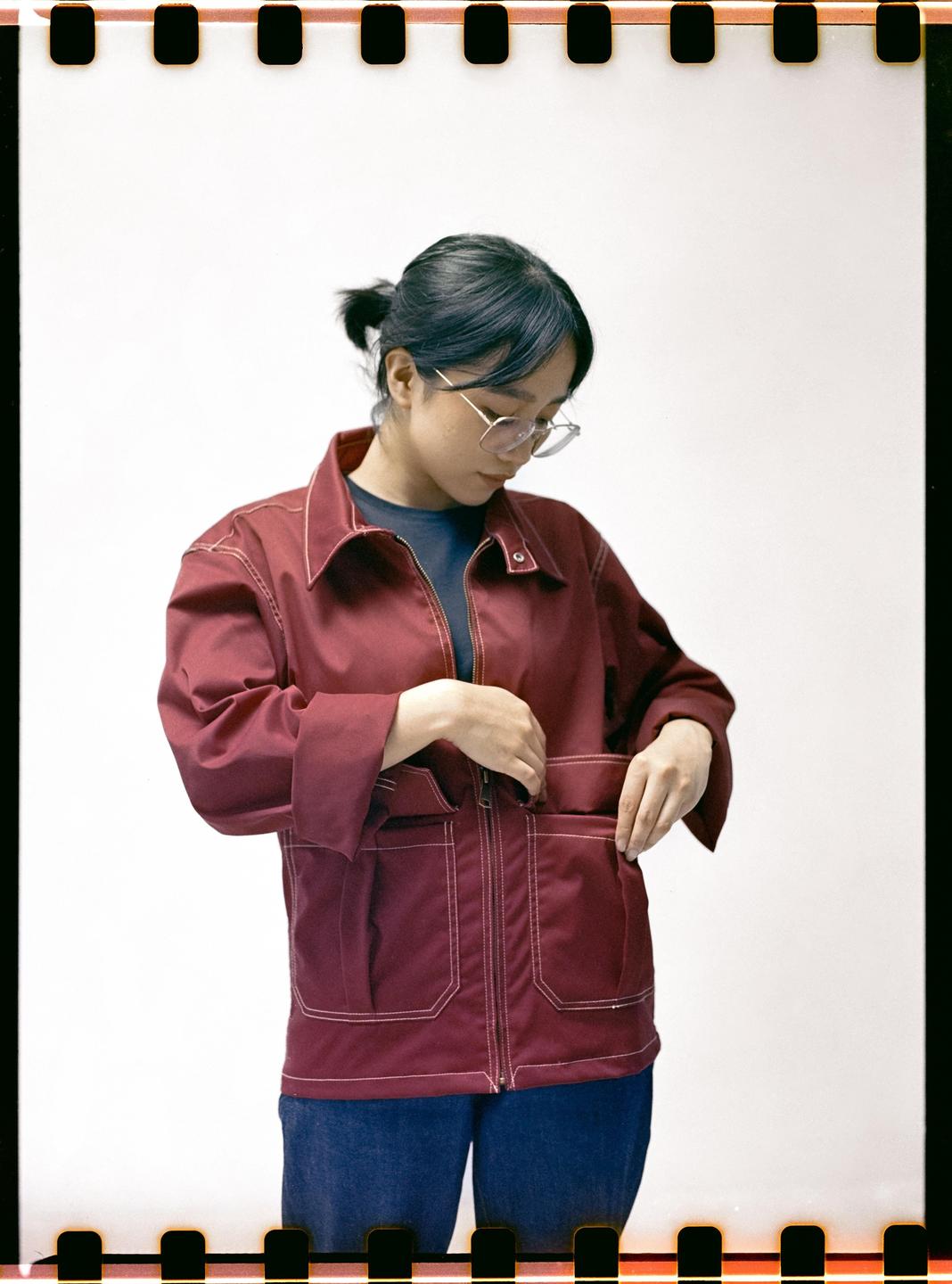 A woman wearing a red jacket and glasses is looking down while adjusting her jacket pocket.