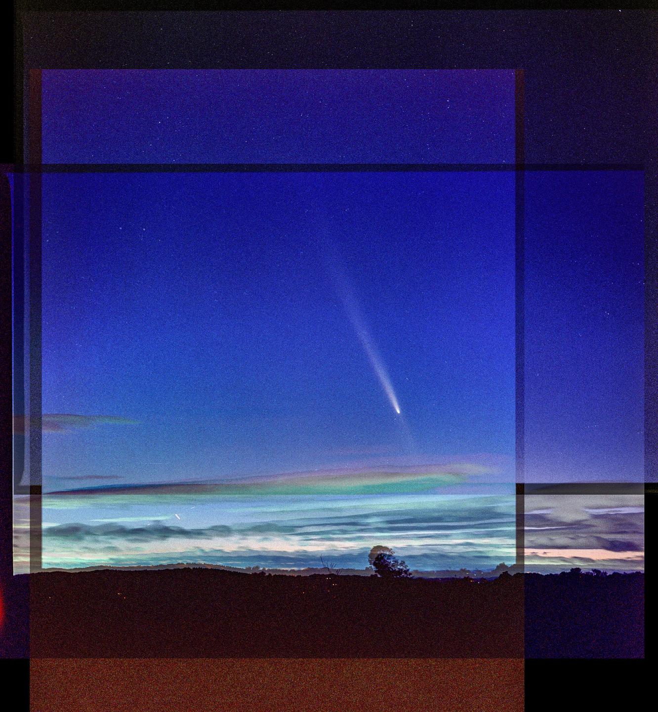 A comet with a bright tail is visible in the night sky above a dark landscape with a single tree.