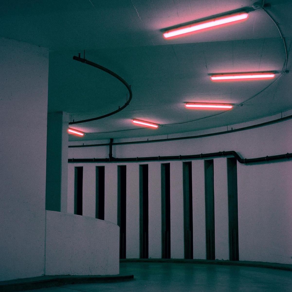 A parking lot with red neon lights on the ceiling and a curved wall.