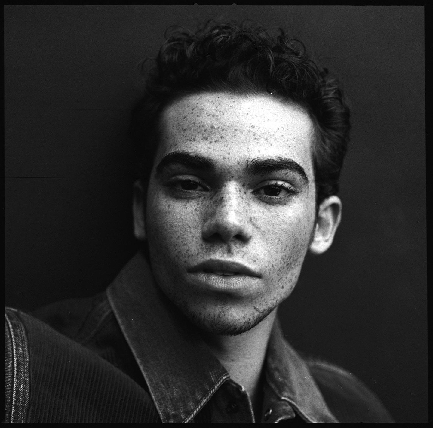 A man with freckles and curly hair looks directly at the viewer.