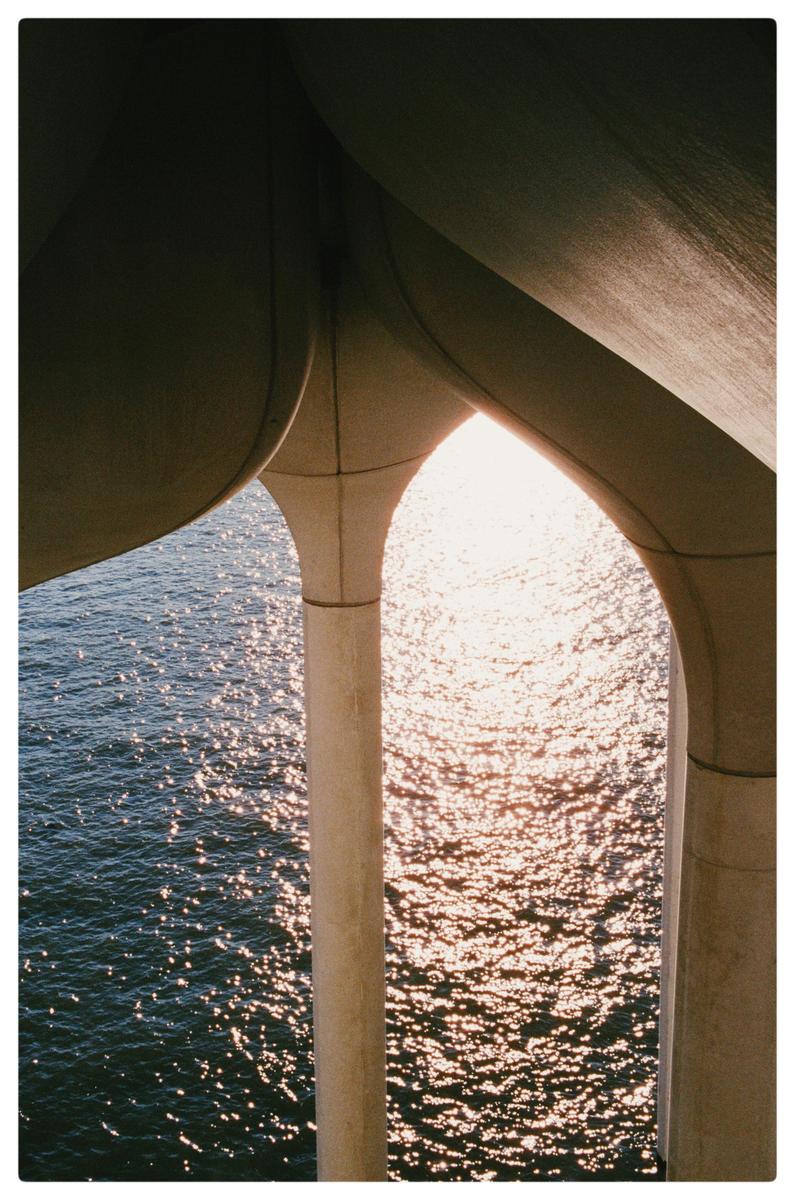 Sunlight reflects off the water under a bridge.