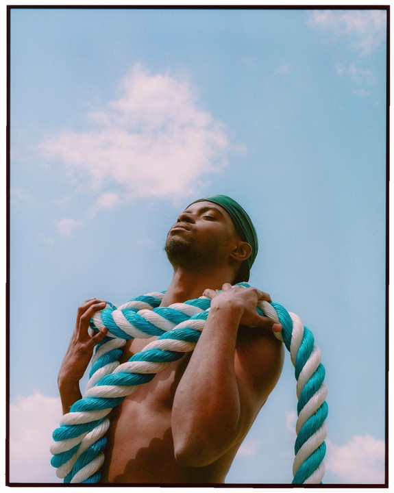 A man with a green durag and a blue and white rope around his shoulders looks up at the sky.