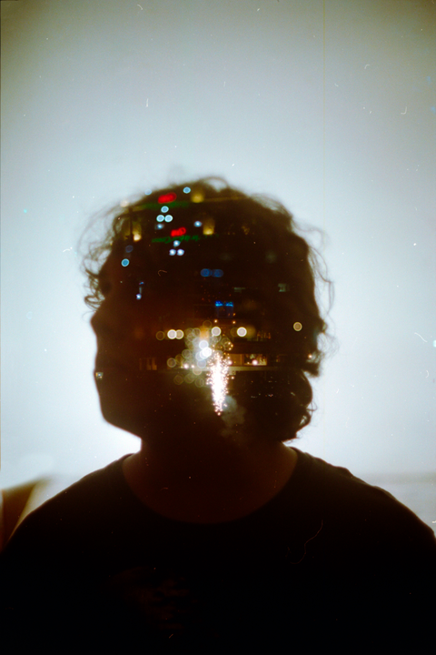 A double exposure shows the silhouette of a person's head and shoulders overlaid with blurred city lights.
