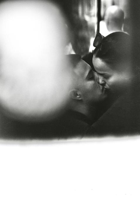 A couple kisses in a blurry, high-contrast black and white street photograph.