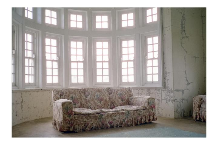 A floral sofa sits in a room with many windows and peeling paint on the walls.