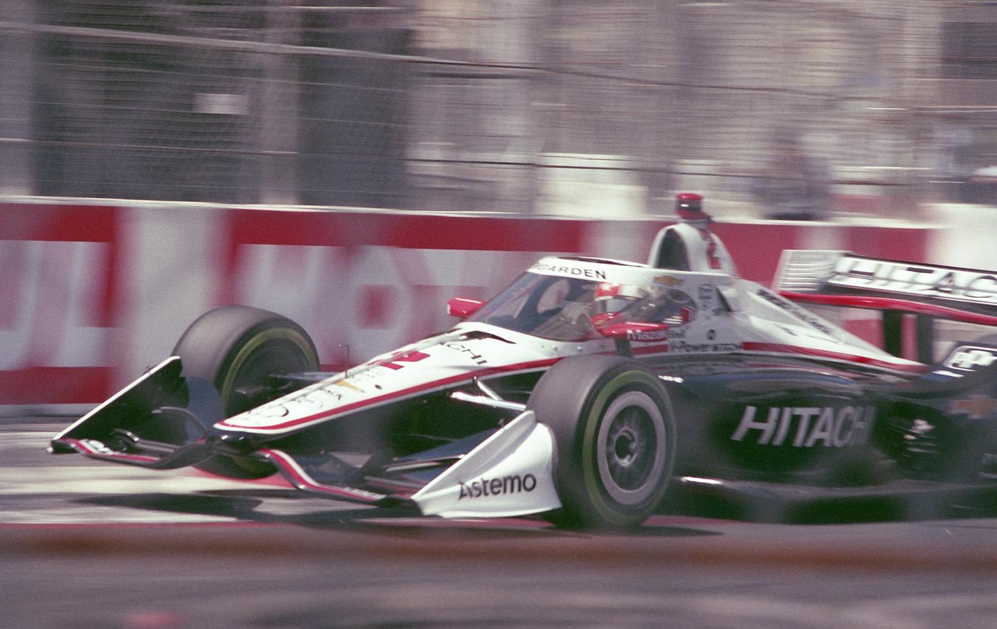A race car speeds past a red and white barrier on a track.