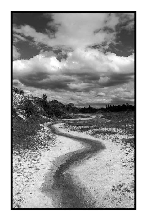 A winding path leads through a sandy landscape under a dramatic cloudy sky.
