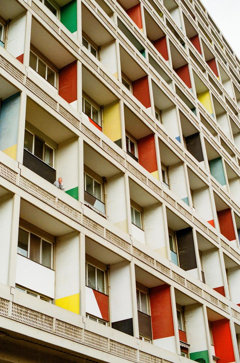 A man stands on a balcony of a building with colorful panels.