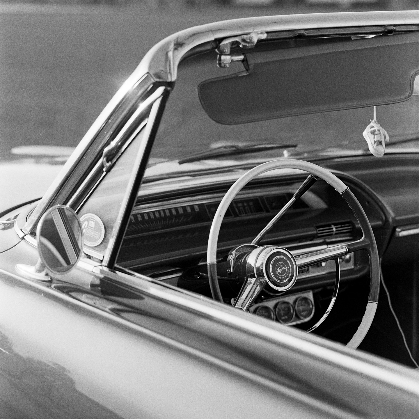 The interior of a vintage convertible car is visible, showing the steering wheel, dashboard, and rearview mirror.