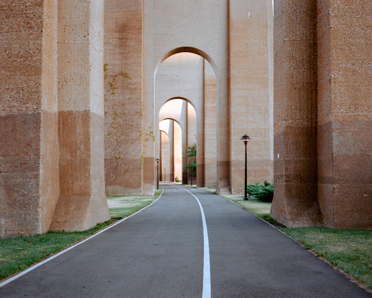 A paved path with a white line runs under a series of large concrete arches.