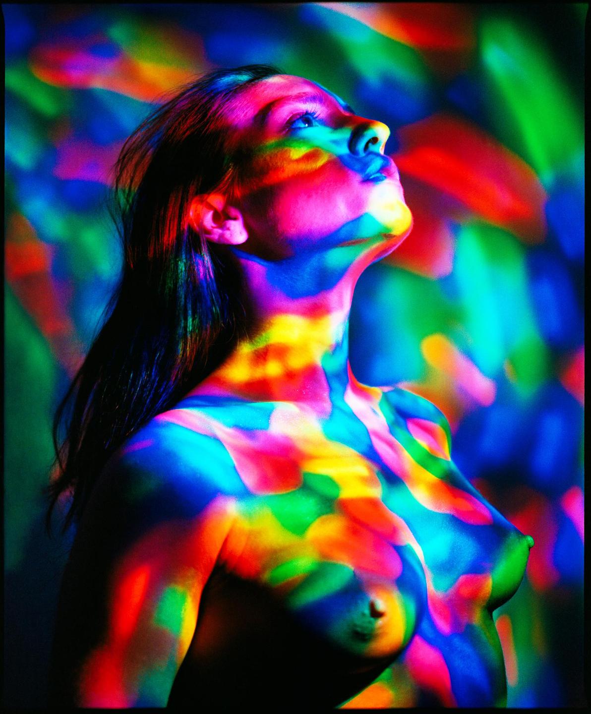 A woman's head and torso are illuminated by colorful light patterns.