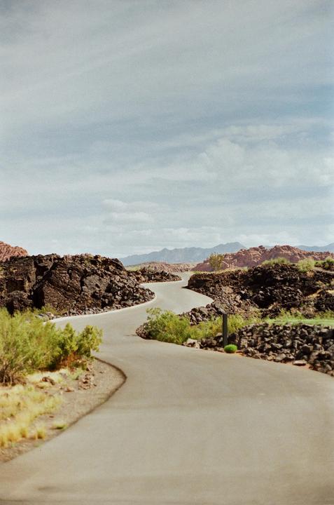 A winding road curves through a rocky, arid landscape under a cloudy sky.