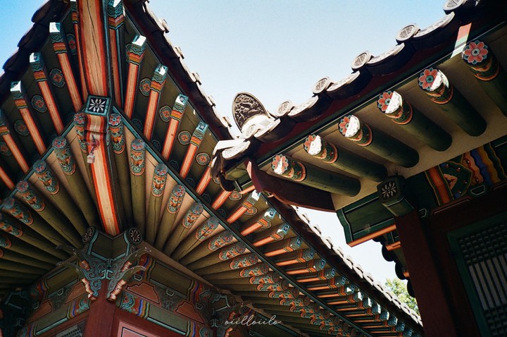 The ornate, colorful roof of a traditional Korean palace is viewed from below against a clear sky.