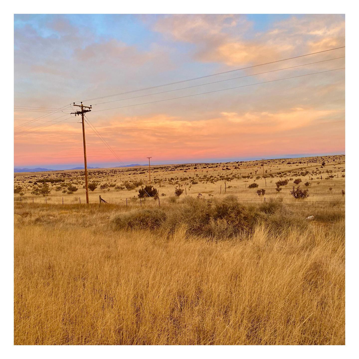 A telephone pole stands in a field of dry grass under a colorful sunset sky.
