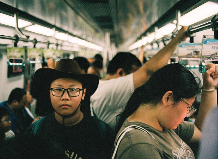 A boy in a cowboy hat and glasses looks directly at the camera while riding a crowded subway.