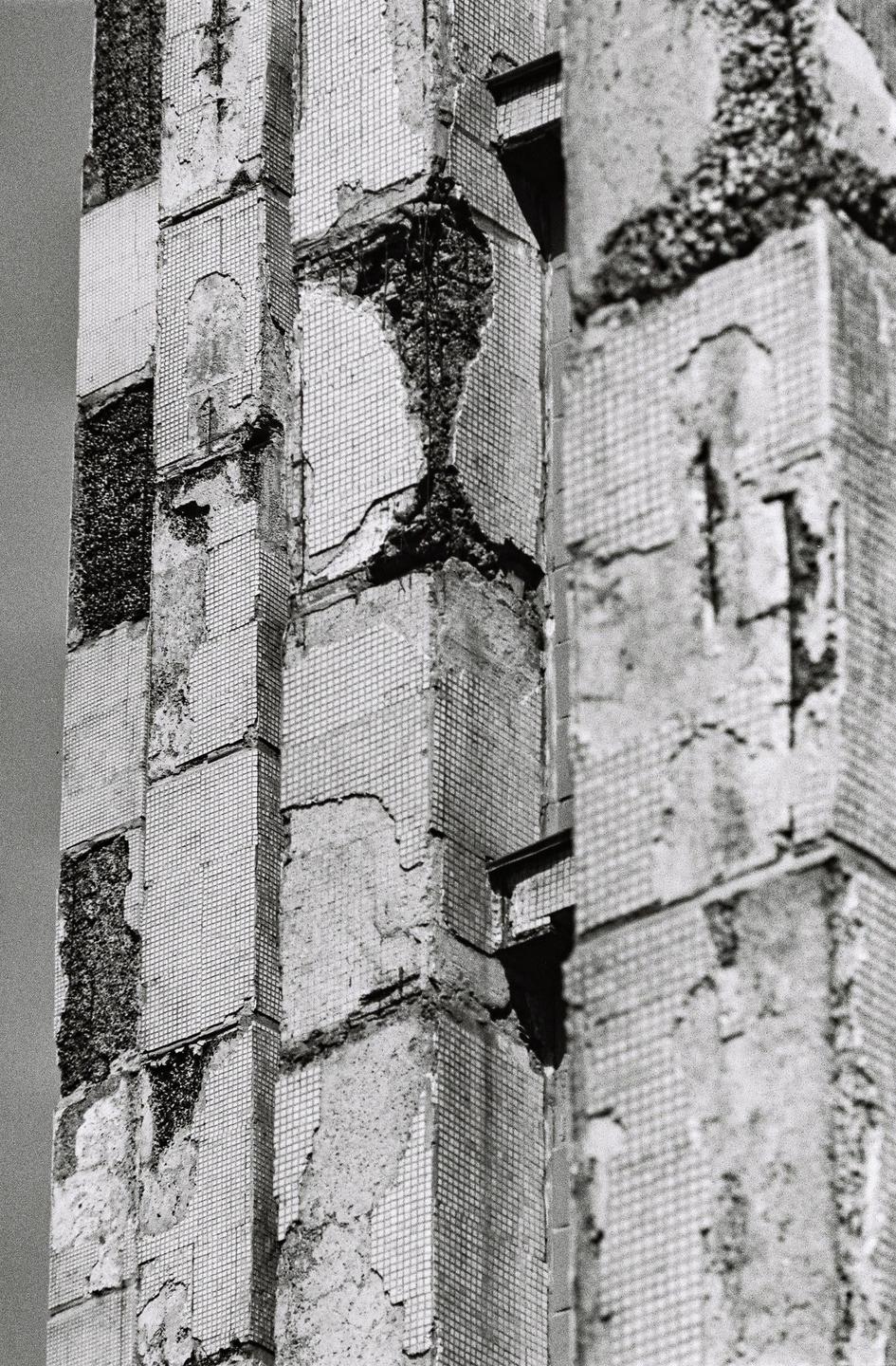 A close-up view shows the decaying facade of a building covered in small square tiles, with large sections of the tiles missing and the underlying concrete exposed.