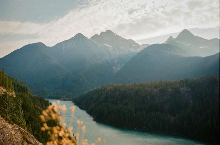 A winding river flows through a valley surrounded by forested mountains under a cloudy sky.
