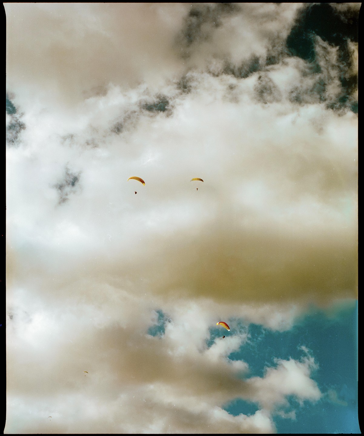 Three paragliders soar through a cloudy sky with patches of blue.