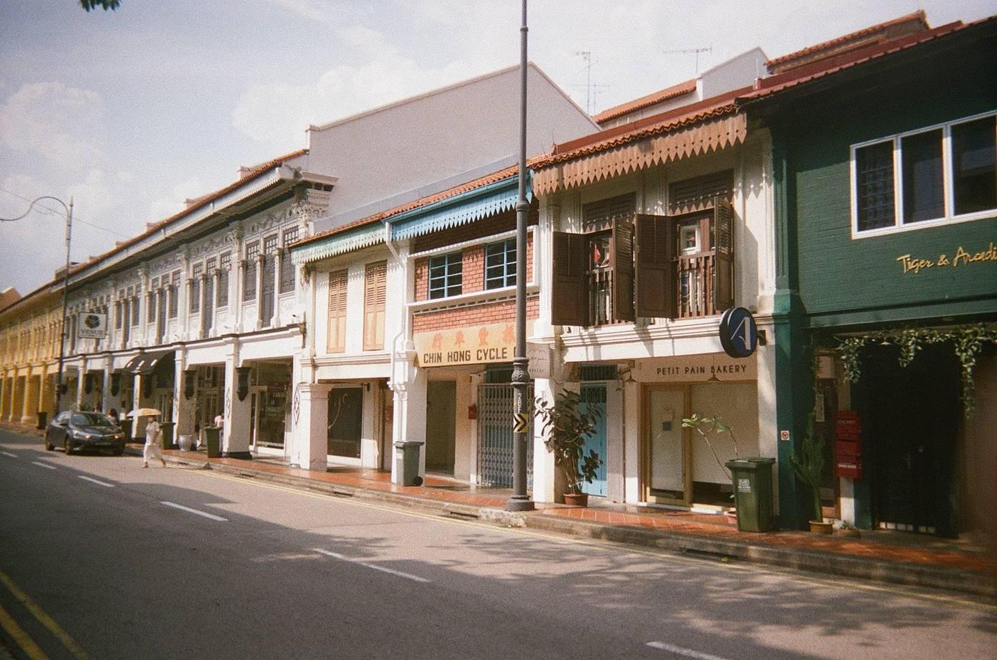 A street lined with colorful shophouses and a car parked on the side of the road.