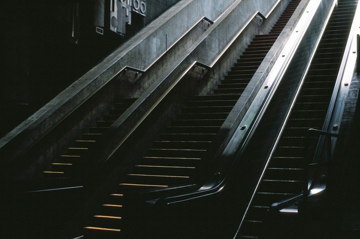 Sunlight illuminates the steps of a dark concrete staircase and escalator.