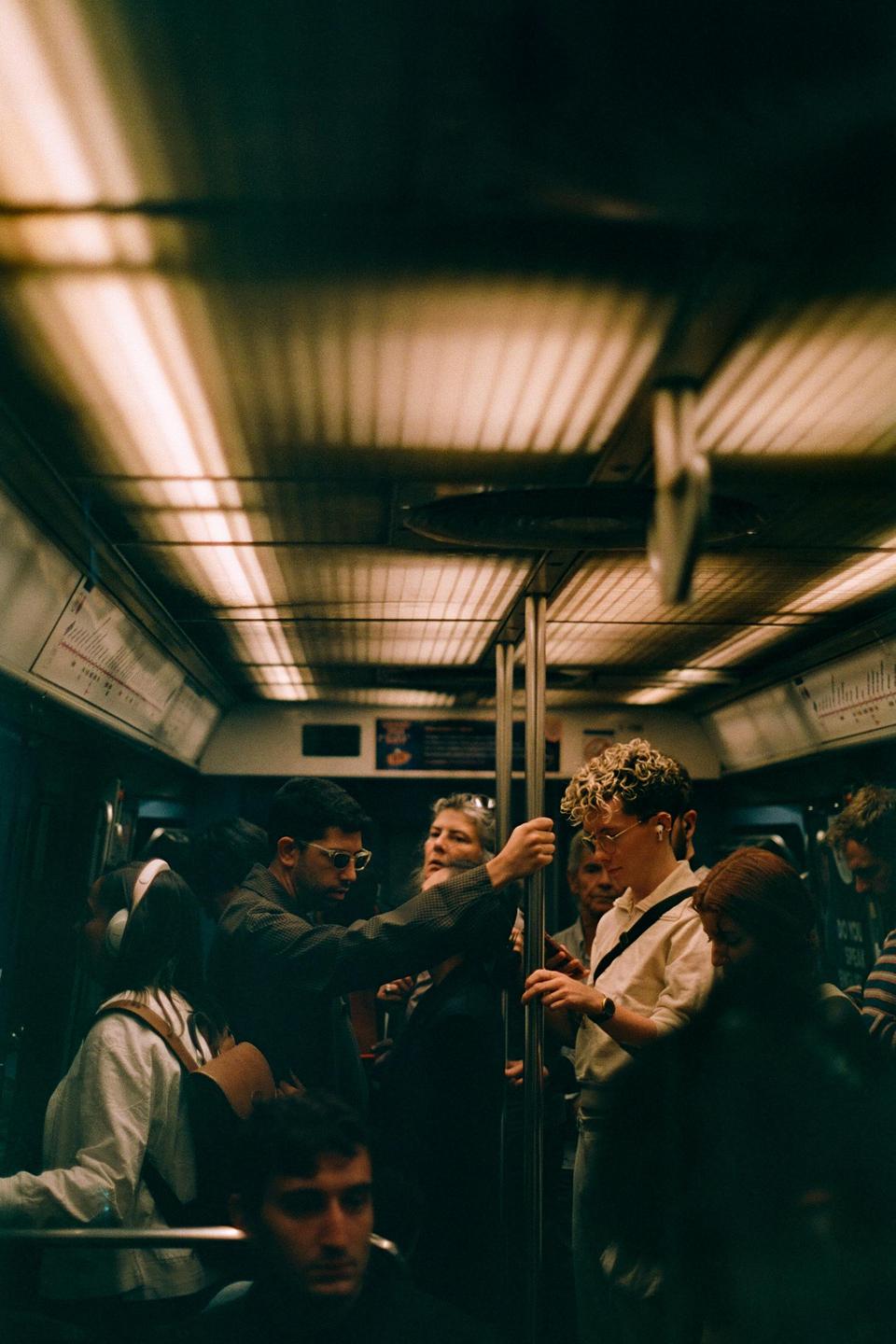 A group of people stand in a subway car, some holding onto poles.