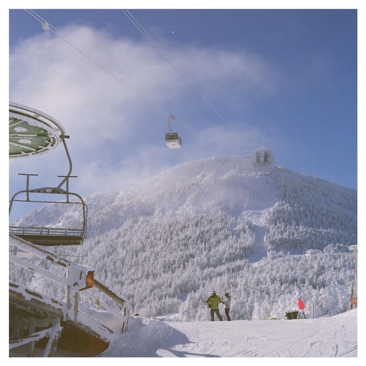 A ski lift and gondola are visible on a snowy mountain with evergreen trees and a few skiers.