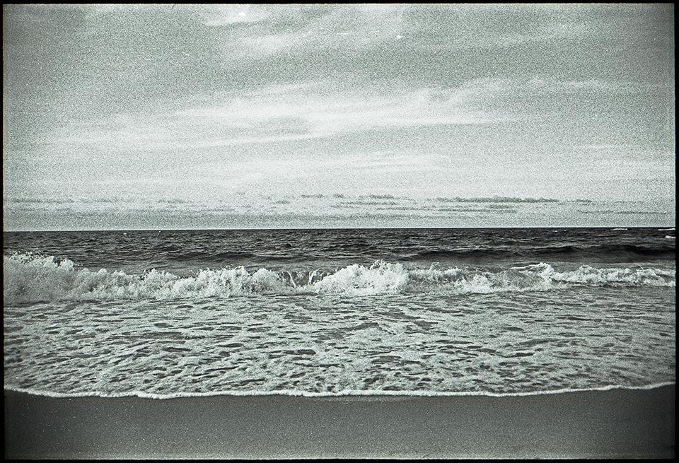 Waves crash onto a sandy beach under a cloudy sky.