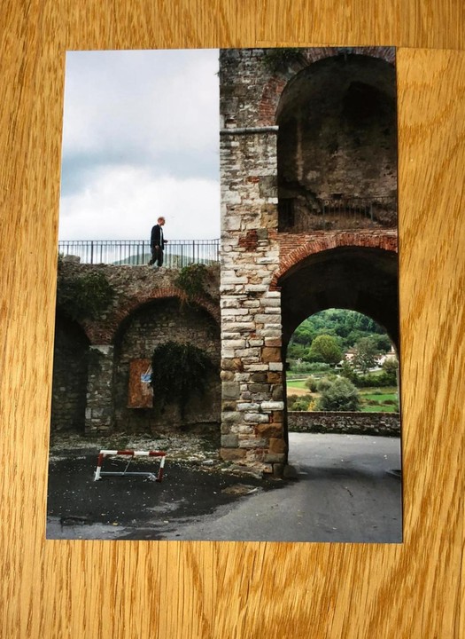 A man walks along a stone wall with arches and a view of a green valley.