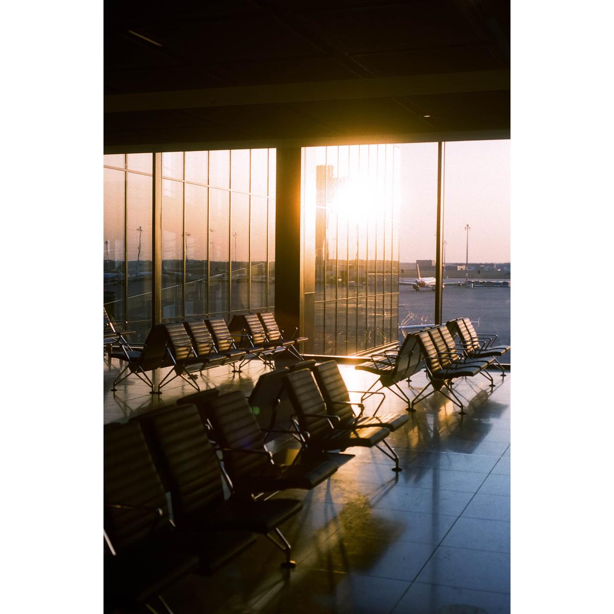 Sunlight streams through large windows into an airport waiting area with rows of empty chairs.