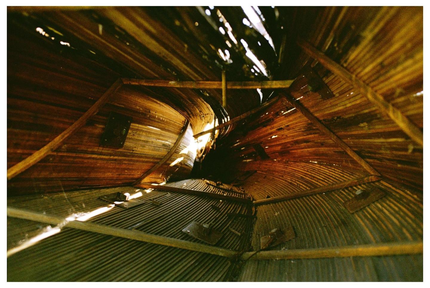 Light streams through holes in the wooden and corrugated metal ceiling of a structure.
