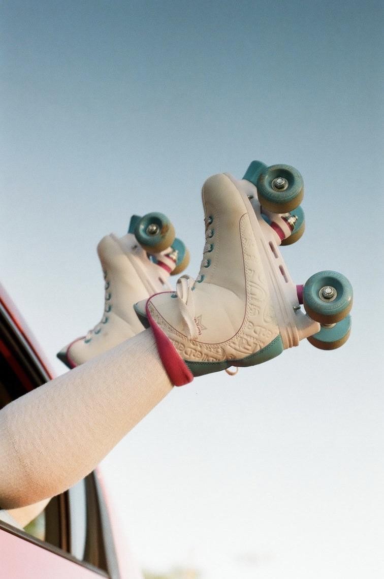 A person's leg with a roller skate on their foot is extended out of a car window against a clear sky.