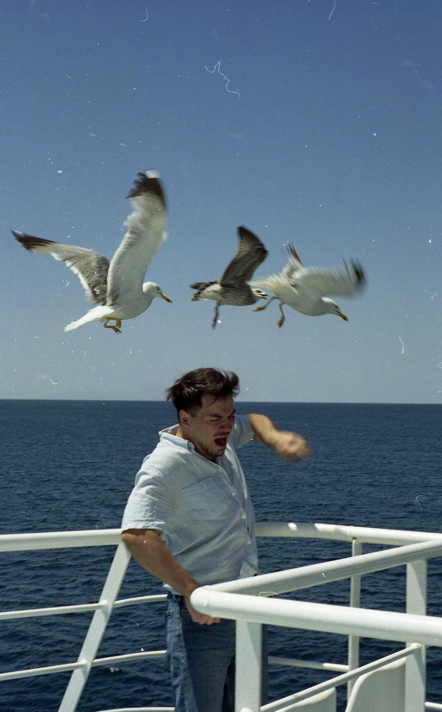 A man on a boat reacts to seagulls flying around him over the ocean.