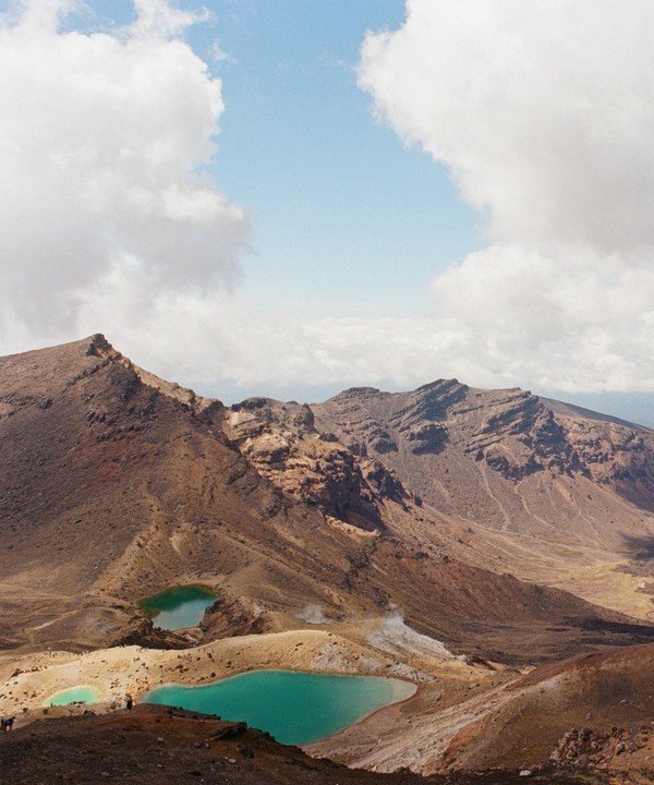 Three emerald lakes are nestled among the brown and tan mountains under a cloudy sky.