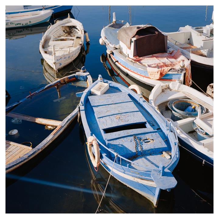 Several small boats are moored in the water, with one blue boat in the foreground and a partially submerged boat to its left.