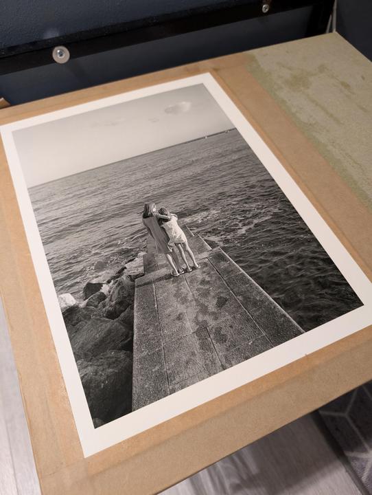 Two women stand on a concrete pier looking out at the ocean.