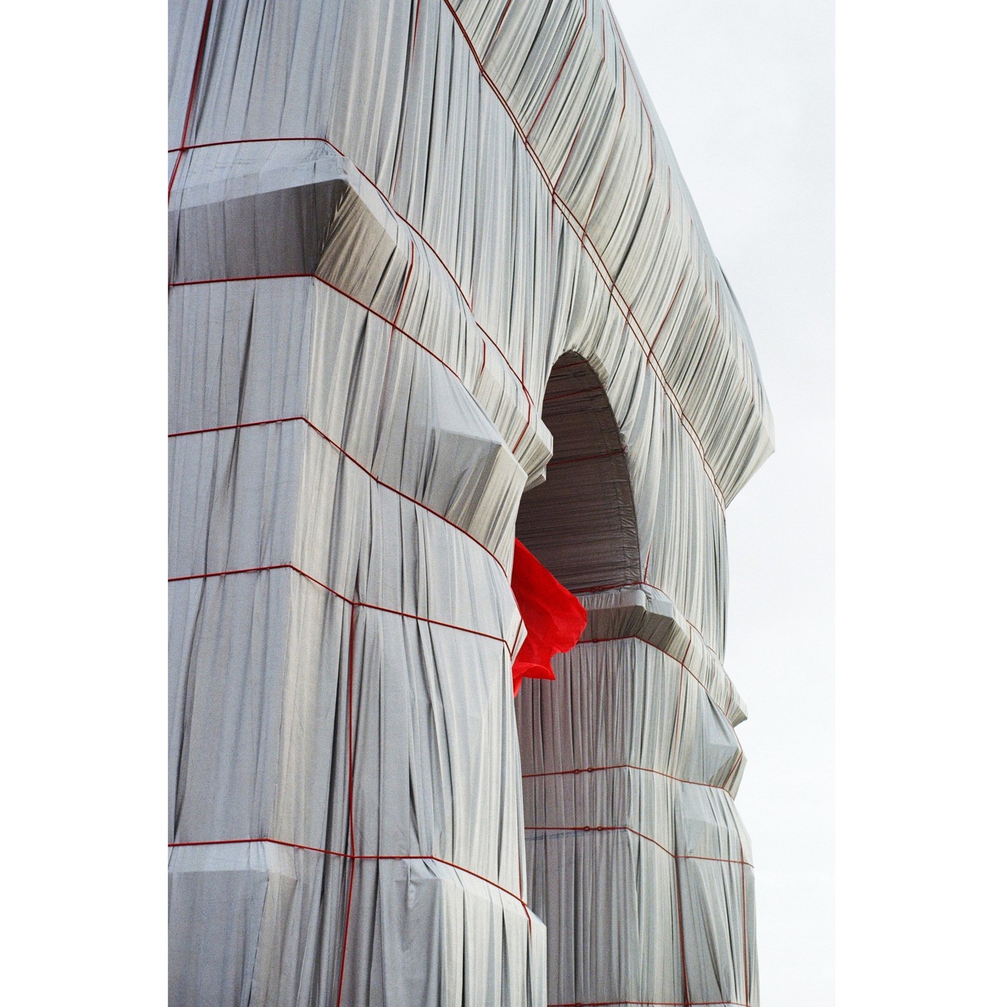 A large monument is wrapped in white fabric and red rope, with a red fabric visible through an archway.