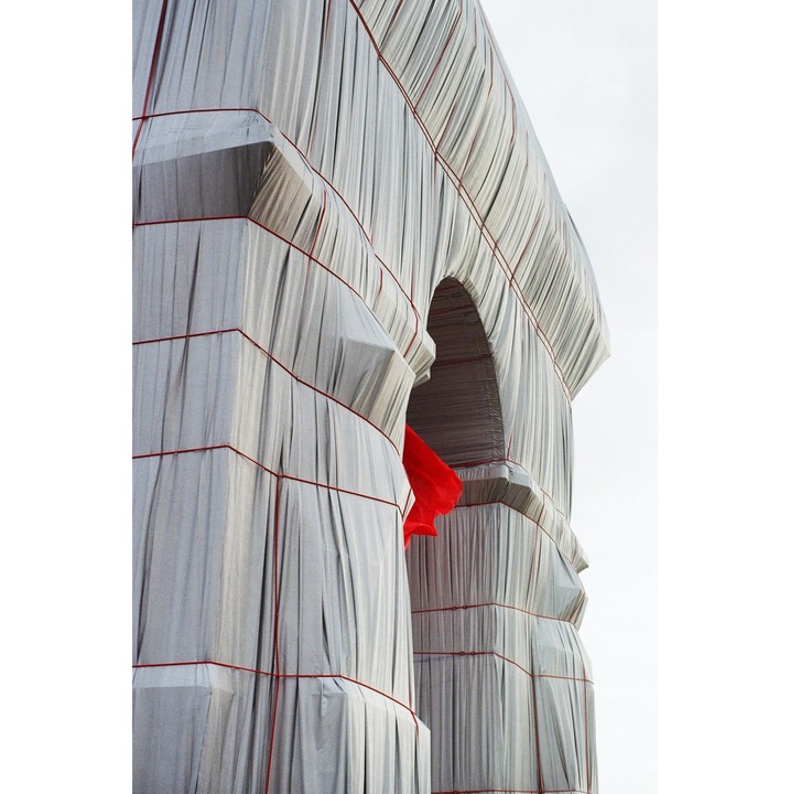A large monument is wrapped in white fabric and red rope, with a red fabric visible through an archway.
