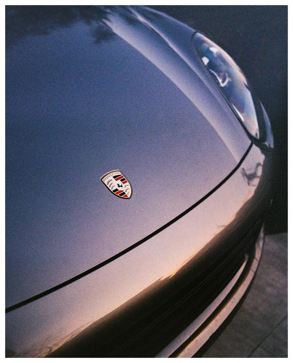 The front of a gray Porsche is visible with its emblem and a reflection of the sunset.
