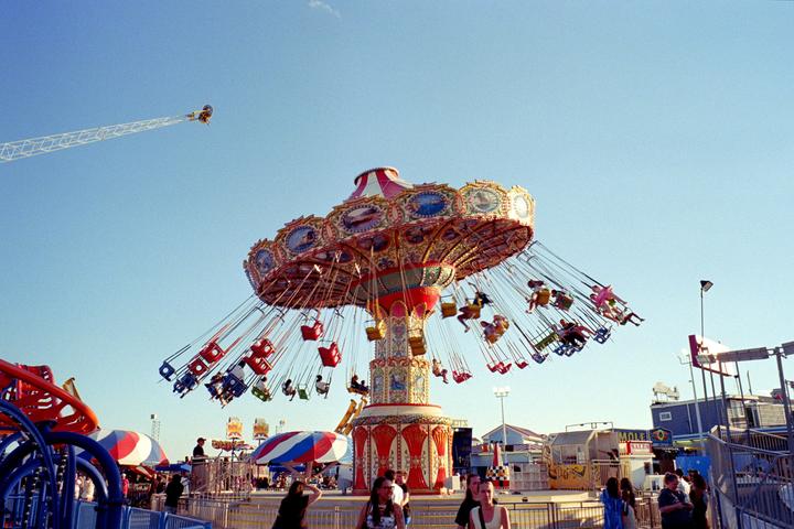 A swing ride at an amusement park is filled with people under a clear blue sky.